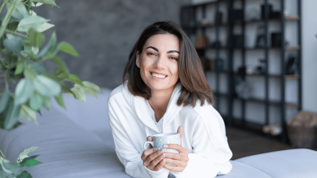 A woman smiling while resting at home with a cup of tea, illustrating the comfortable recovery process after labiaplasty.
